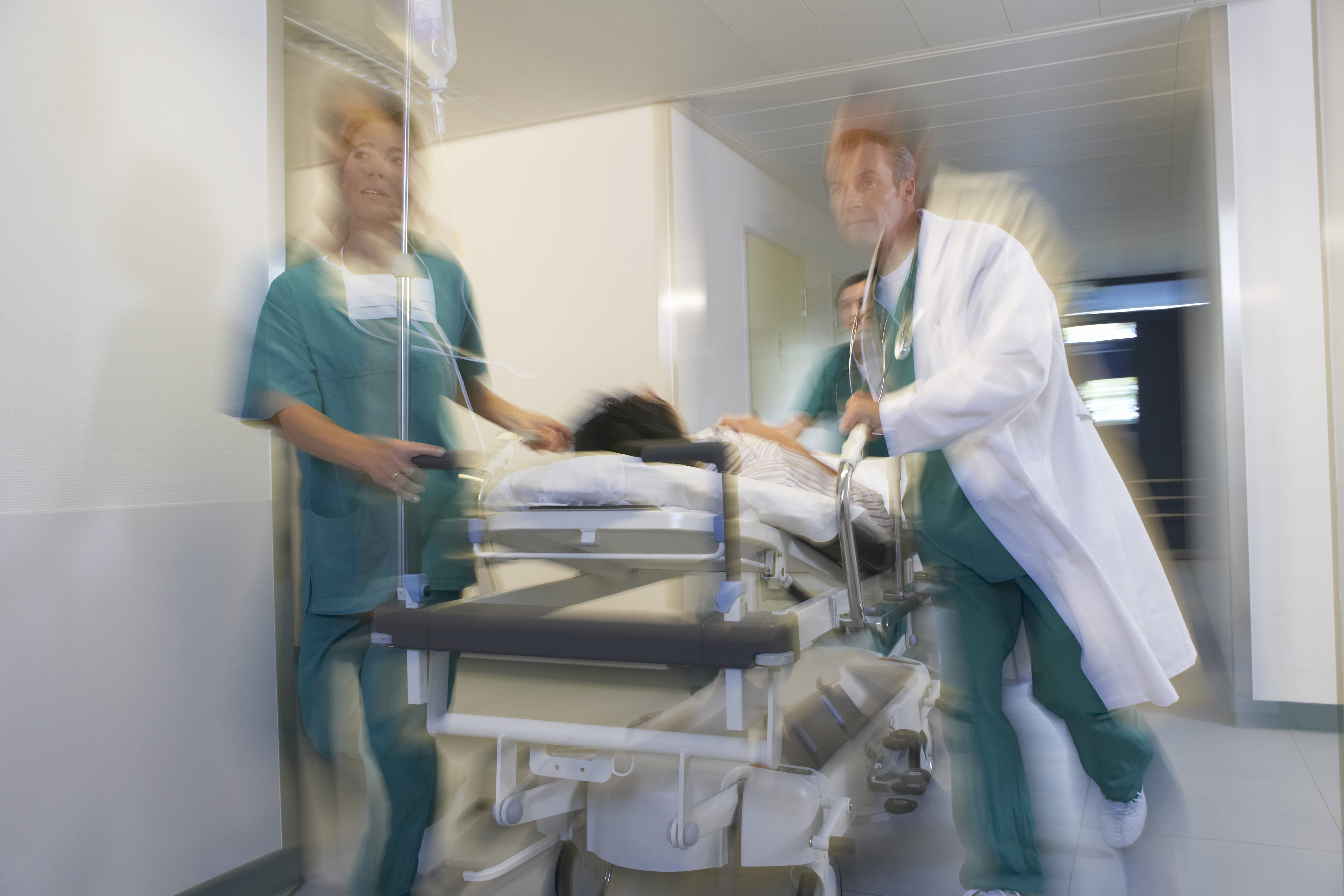 3 Doktoren transportieren einen Patienten auf einer Liege in den OP-Saal.