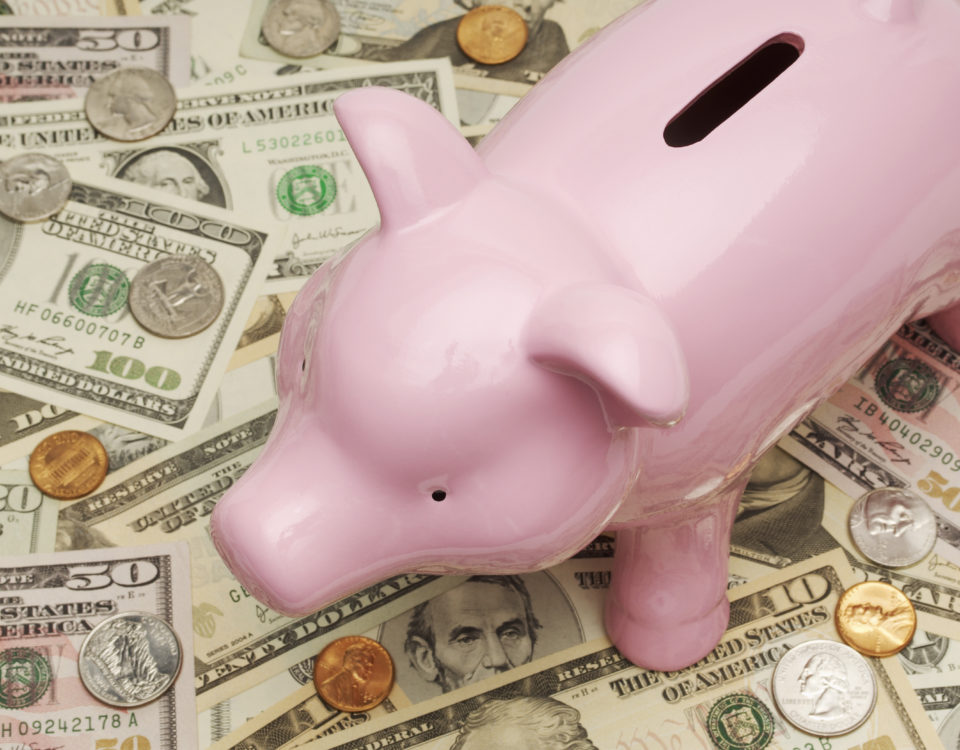 Ein Sparschwein steht auf Dollarscheinen.